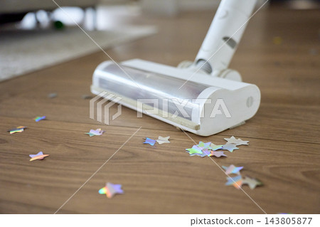 Vacuum cleaner picking up colorful star shaped confetti from wooden floor Vacuum cleaner picking up colorful star shaped confetti from wooden floor 143805877