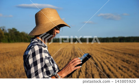 Adult farmer using digital tablet at wheat meadow on sunny day. Female agronomist monitoring harvest at barley field. Beautiful scenic landscape. Concept of agricultural business. Slow motion Adult farmer using digital tablet at wheat meadow on sunny day. Female agronomist monitoring harvest at barley field. Beautiful scenic landscape. Concept of agricultural business. Slow motion 143805920