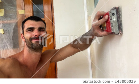 POV of young man uses brush to clean finished wall surface removing dust and small imperfections after renovation work. Male worker carefully prepare smooth wall for next finishing stage inside room 143806029