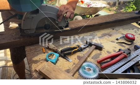 Arms of professional repairman sawing wooden construction with a circular saw at construction. Male hands of adult craftsman cuts wood using electric grind wheel at the site. Slow motion Arms of professional repairman sawing wooden construction with a circular saw at construction. Male hands of adult craftsman cuts wood using electric grind wheel at the site. Slow motion 143806032