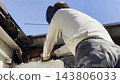 Manual laborer in protective mask welds iron detail at construction. Professional young repairman with welding machine working at the site. Male welder operating with metal on house. Close up 143806033