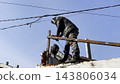 Young mechanic in protective gloves polishing iron using electric grinder wheel at construction. Professional repairman grinding metal details with circular saw on house at sunny day. Slow mo 143806034
