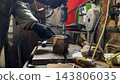 Male hands in protective gloves of mechanic operate a drill press while machining a metal detail at garage. Repairman works carefully in a small workshop, concentrating on technical repair. Close up 143806035
