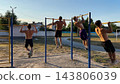 Group of strong sporty men doing pull ups on horizontal bar at sports ground. Young shirtless sportsmen exercising at nature. Muscular athletes training outdoor. Healthy and active lifestyle concept 143806039