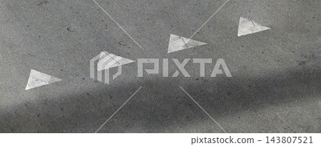 Four worn white triangle road markings pointing right on gray asphalt with a soft shadow, urban street pavement texture with copy space, high angle view and diagonal composition Four worn white triangle road markings pointing right on gray asphalt with a soft shadow, urban street pavement texture with copy space, high angle view and diagonal composition 143807521