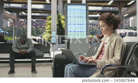 Laptop, woman traveler and typing take focus as passenger works on computer beside suitcase in coach station. Remote work, mobile productivity and flexible schedules turn waiting time into work. Laptop, woman traveler and typing take focus as passenger works on computer beside suitcase in coach station. Remote work, mobile productivity and flexible schedules turn waiting time into work. 143807644