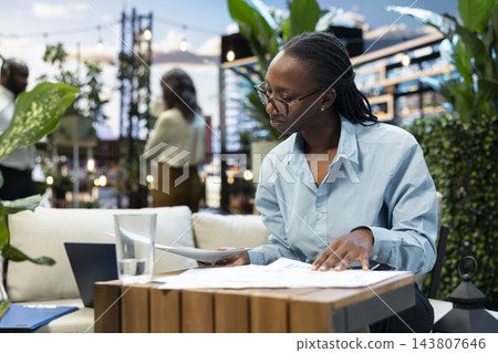 Documents, businesswoman and analysis lead as professional studies paperwork beside an open laptop. Planning, research and decision making support focused project review in a leafy rooftop lounge. Documents, businesswoman and analysis lead as professional studies paperwork beside an open laptop. Planning, research and decision making support focused project review in a leafy rooftop lounge. 143807646