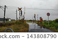 A railroad crossing wet from the rain and a road with puddles. 143808790