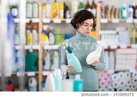 Adult woman chooses cleaning spray in store Adult woman chooses cleaning spray in store 143809373