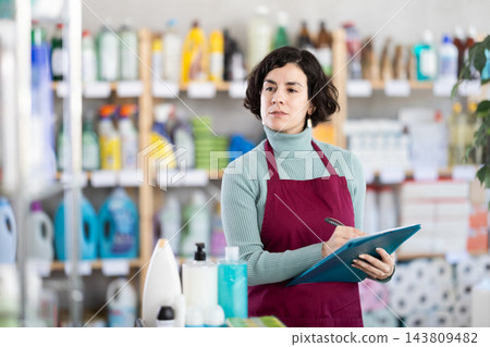 Middle-aged woman taking record of inventory in household store Middle-aged woman taking record of inventory in household store 143809482