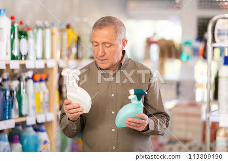 Male shopper carefully selects a spray glass cleaner for windows in home Male shopper carefully selects a spray glass cleaner for windows in home 143809490