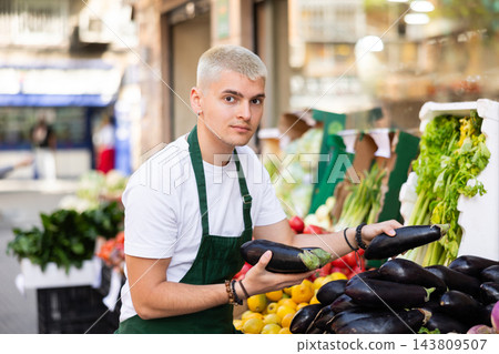 Guy shop seller puts eggplant goods on display case 143809507
