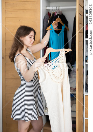 Young woman choosing which dress to wear Young woman choosing which dress to wear 143809508