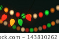 Close-up of a hanging retro Christmas light bulb in red, gold, and green against a holiday background. 143810262
