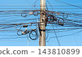 Concrete utility pole overloaded with a messy tangle. Which consists of communication telephone and electrical cables against a clear blue sky background. 143810899