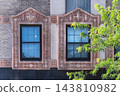 Two Windows with Ornate Floral Surrounds on a Brick Facade 143810982