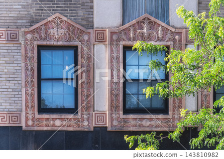 Two Windows with Ornate Floral Surrounds on a Brick Facade 143810982