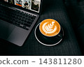 Hot coffee latte art in cup on saucer beside laptop on dark table 143811280
