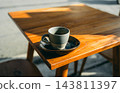 Hot espresso in a rustic ceramic cup on a wooden table with morning sunlight and hard shadows 143811397