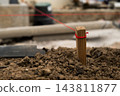 A wooden stake secured with red string stands in soil, indicating layout on a construction site. A closeup of the marked stake among dirt and construction materials. 143811877