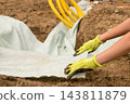 Freshly turned soil lines a trench as protective fabric is spread out for drainage system installation. Visible yellow hoses and tools indicate an active construction site focused on water management. 143811879