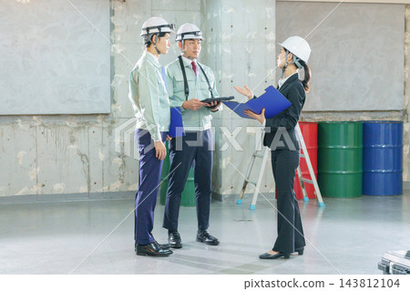 三名年輕的日本工人,兩男一女,正在建築工地開會。 三名年輕的日本工人,兩男一女,正在建築工地開會。 143812104