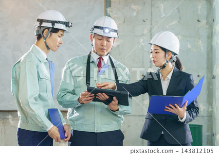 三名年輕的日本工人,兩男一女,正在建築工地一邊看著平板電腦一邊開會。 三名年輕的日本工人,兩男一女,正在建築工地一邊看著平板電腦一邊開會。 143812105
