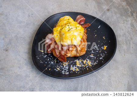 Croissant sandwich with scrambled eggs and crispy bacon on a black plate Croissant sandwich with scrambled eggs and crispy bacon on a black plate 143812624