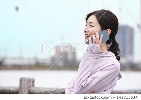 一位中年婦女身穿運動服,邊走邊用智慧型手機通話。 一位中年婦女身穿運動服,邊走邊用智慧型手機通話。 143813634