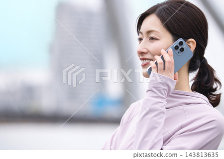 A middle-aged woman talking on her smartphone while walking in sportswear. A middle-aged woman talking on her smartphone while walking in sportswear. 143813635