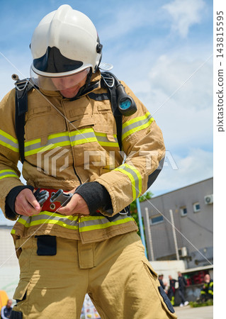 Firefighter In Full Protective Gear Adjusting Safety Harness And Belt During Training Or Emergency Response Firefighter In Full Protective Gear Adjusting Safety Harness And Belt During Training Or Emergency Response 143815595