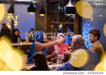 Family and Friends Sharing Holiday Gift Exchange Around a Cozy Restaurant Table With Warm Lighting Family and Friends Sharing Holiday Gift Exchange Around a Cozy Restaurant Table With Warm Lighting 143816104