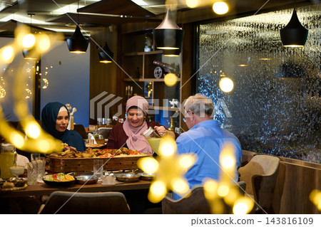 Multigenerational Family Dinner In Restaurant With Hijab-Wearing Women Sharing A Festive Meal Multigenerational Family Dinner In Restaurant With Hijab-Wearing Women Sharing A Festive Meal 143816109