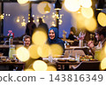 Smiling Family Enjoying Warm Restaurant Dinner Celebration With Woman in Headscarf and Friends 143816349