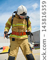 Firefighter In Full Protective Gear Adjusting Safety Belt During Rooftop Training Drill On Sunny Day 143816359