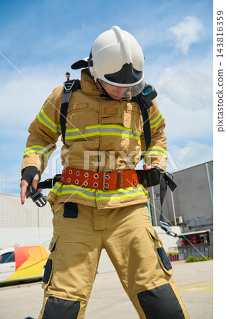 Firefighter In Full Protective Gear Adjusting Safety Belt During Rooftop Training Drill On Sunny Day 143816359
