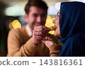 Couple Sharing Food During Romantic Date Night With Woman in Hijab and Warm Bokeh Lights 143816361