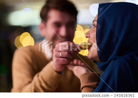 Couple Sharing Food During Romantic Date Night With Woman in Hijab and Warm Bokeh Lights Couple Sharing Food During Romantic Date Night With Woman in Hijab and Warm Bokeh Lights 143816361
