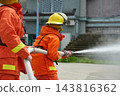 Firefighters Working Together With Hose During Firefighting Training Wearing Orange Protective Gear And Helmets 143816362