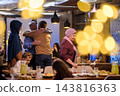 Multi-Generational Muslim Family Hugging at Festive Dinner Reunion With Warm Lights and Food 143816363