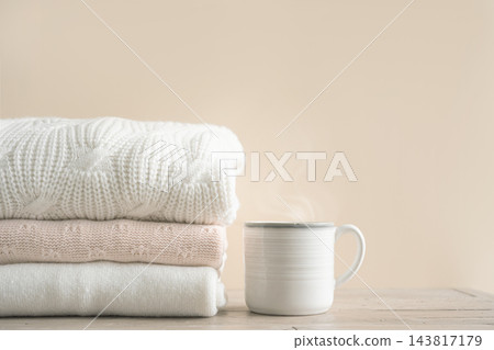 Stack of folded knitted sweaters with cup of coffee Stack of folded knitted sweaters with cup of coffee 143817179