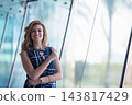 Confident smiling businesswoman standing by glass windows in modern office building, professional and approachable 143817429