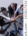 Business team joining hands in a diverse office showing teamwork and unity across generations 143817432