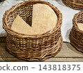 Cheese wheels displayed in a wicker basket on a wooden surface 143818375
