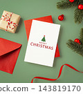 Merry christmas text on white card with red envelop, gift box, red ribbon and xmas decoration on green background 143819170