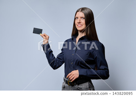Smiling businesswoman holding black credit card on studio gray background Smiling businesswoman holding black credit card on studio gray background 143820095