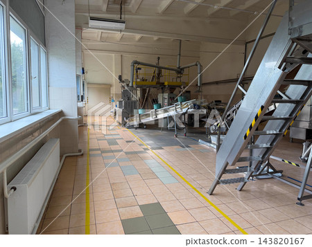 Inclined metal conveyors and tubular feeding equipment stand inside a food processing factory, illustrating industrial product handling and transfer Inclined metal conveyors and tubular feeding equipment stand inside a food processing factory, illustrating industrial product handling and transfer 143820167