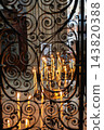 Votive candles burning behind ornate wrought iron gate in a historic church in France, creating a spiritual atmosphere with warm glowing light 143820388