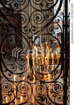 Votive candles burning behind ornate wrought iron gate in a historic church in France, creating a spiritual atmosphere with warm glowing light 143820388