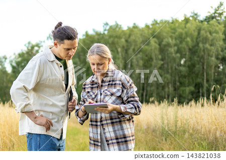 Two diverse agronomists working together with a digital tablet in a mature wheat field. Concept of smart farming, mentorship and family agricultural business. 143821038
